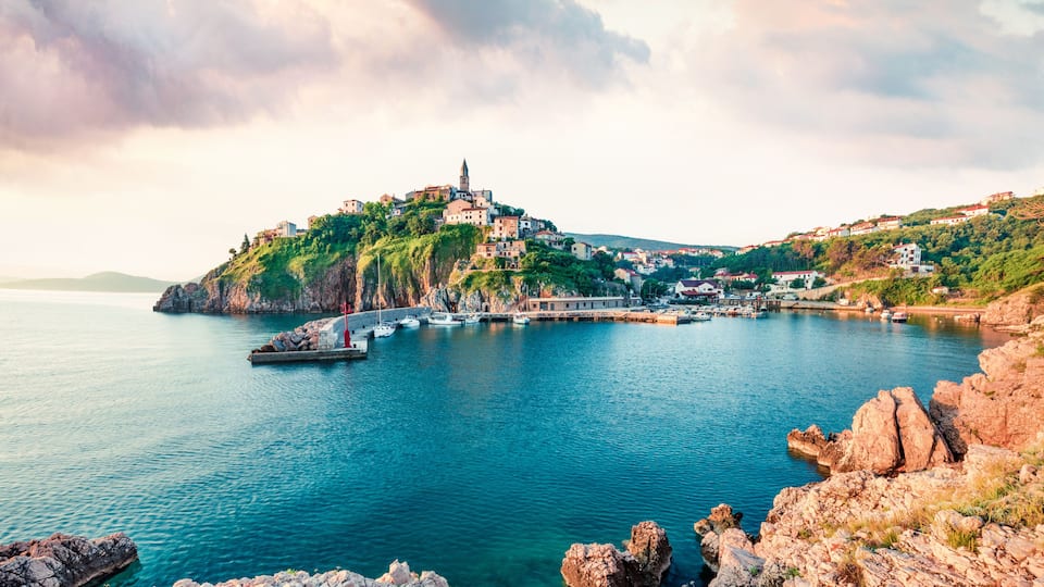 A coastal town with a prominent church on a hill, a harbor with boats, and rocky terrain.