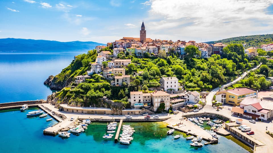 A coastal town with a prominent tower, lush greenery, and a marina with boats.