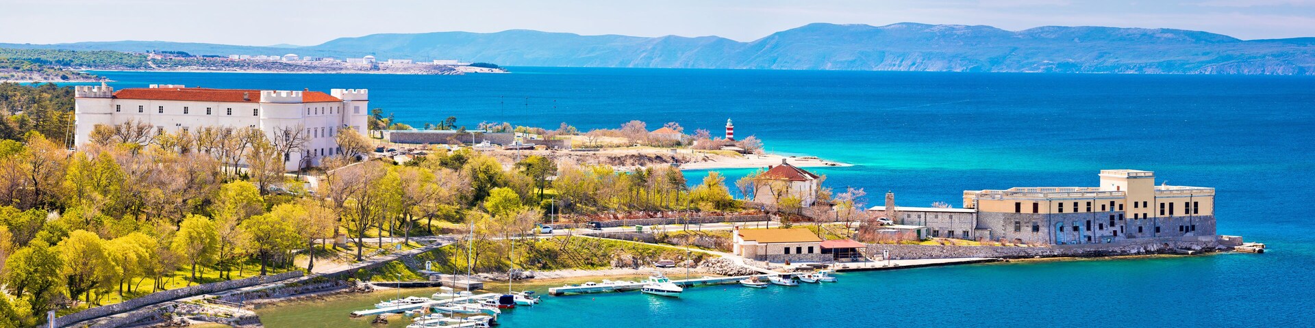 A coastal town with a castle, a lighthouse, and boats docked at the harbor.