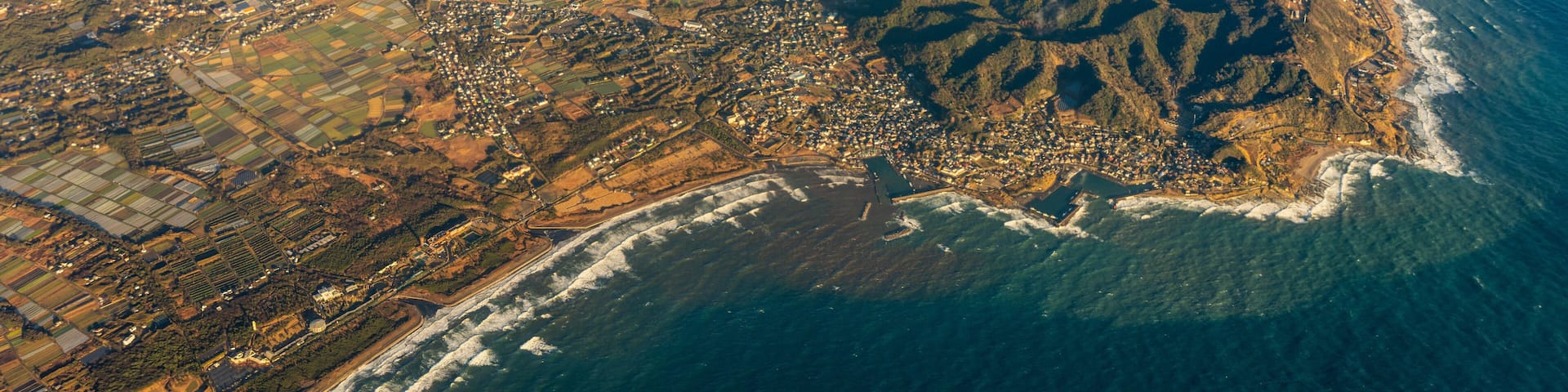 An aerial view of a coastal region with a mix of urban areas, agricultural fields, and rugged terrain.