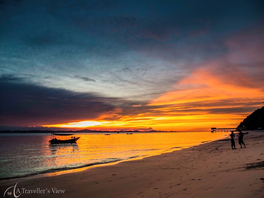 Un atardecer sobre una playa con barcos y gente.