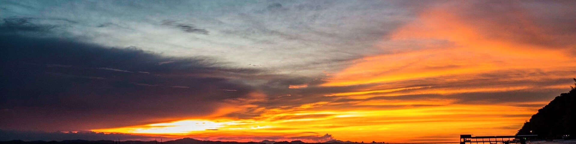 Un atardecer sobre una playa con barcos y gente.