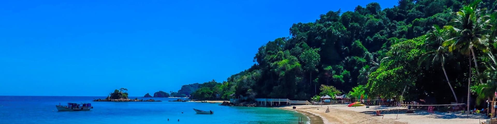 A beach with clear turquoise water, several boats anchored near the shore, and rocky outcrops.