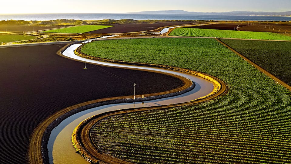 An aerial view of a large agricultural field with a winding water channel.