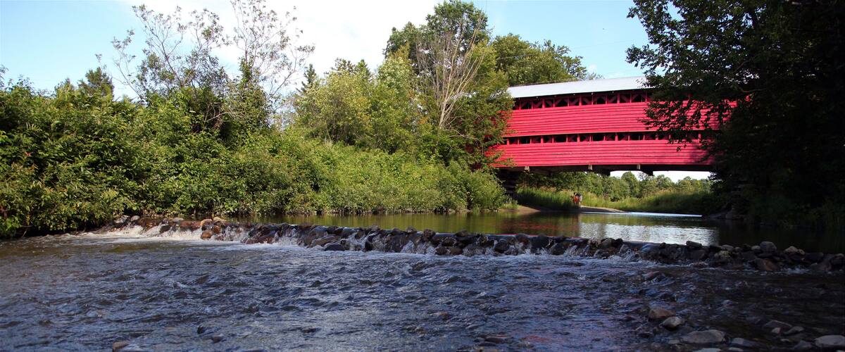 A river with rocks and a red covered bridge in the background.