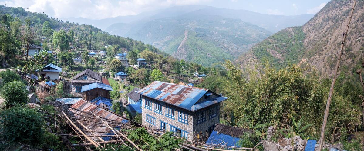 A mountainous village with traditional houses, lush greenery, and distant hills.