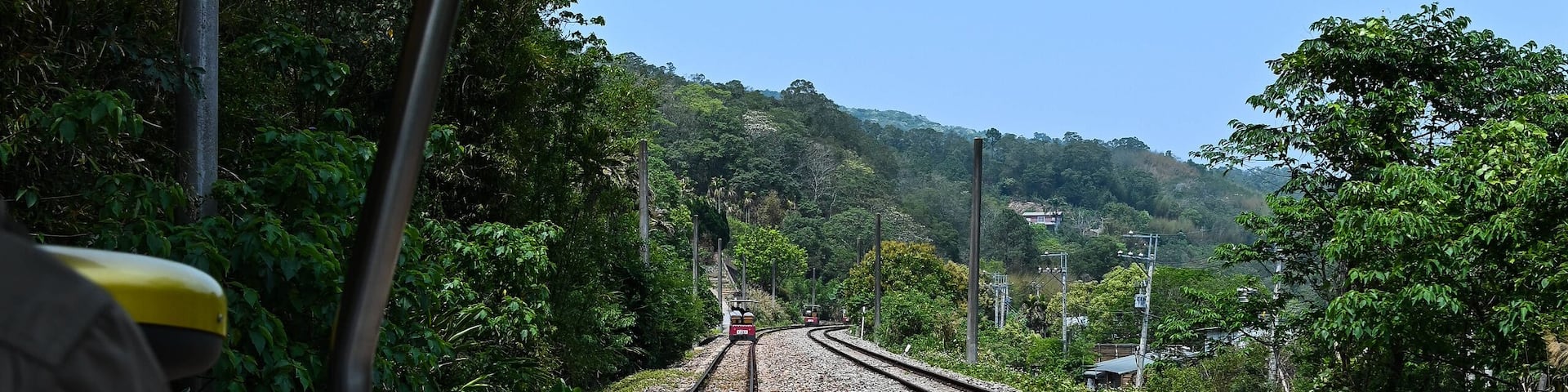Una vía de tren con un vagón, rodeado de vegetación y colinas al fondo.