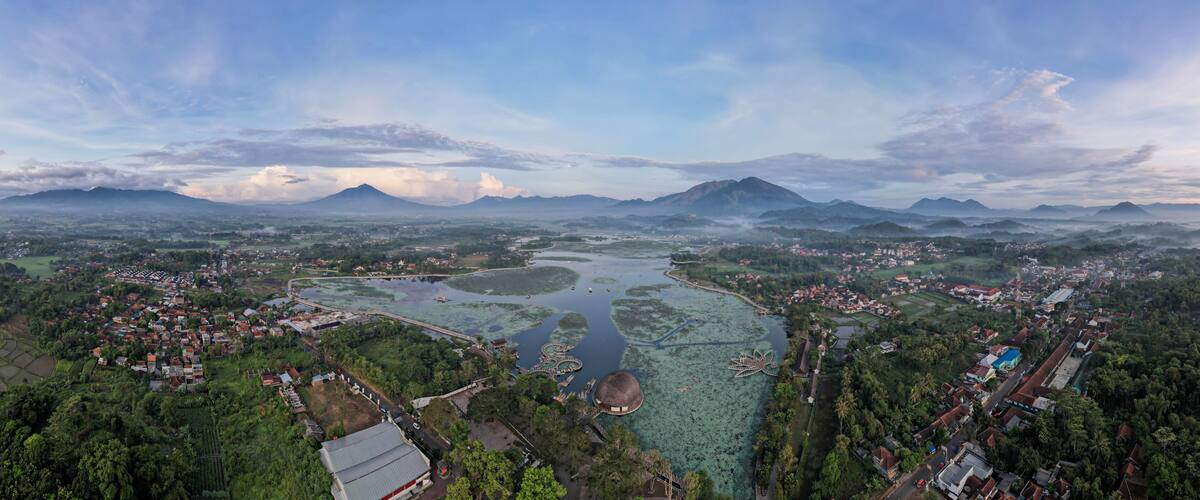 An aerial view of a coastal town with a river, surrounding greenery, and distant mountains.