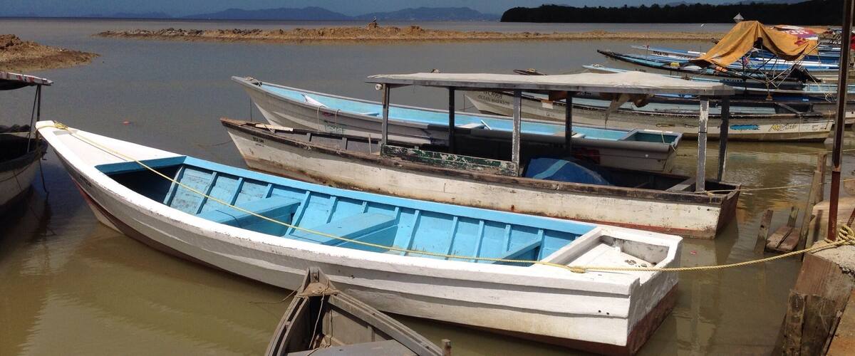 A row of small boats docked at a calm river with a clear sky above.