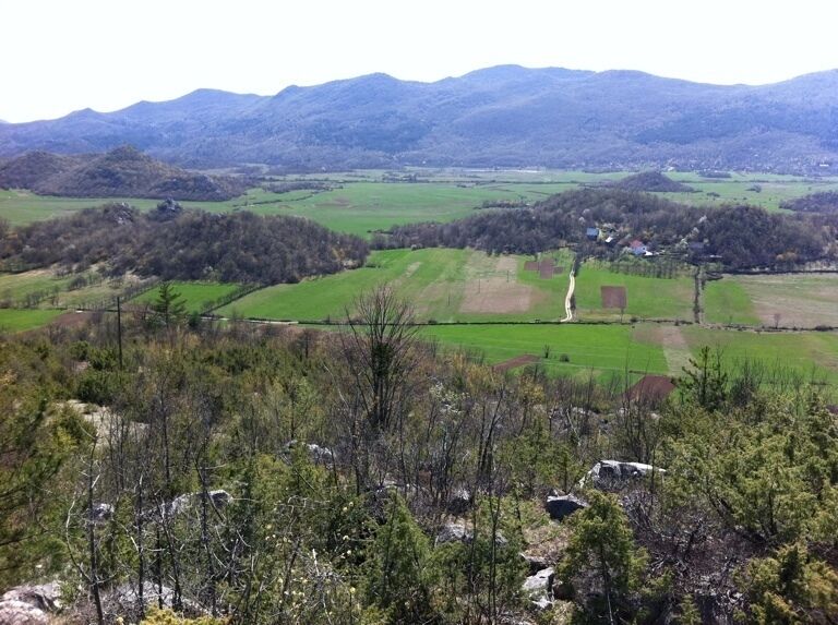 A mountainous landscape with green fields, a winding road, and a small settlement in the valley.