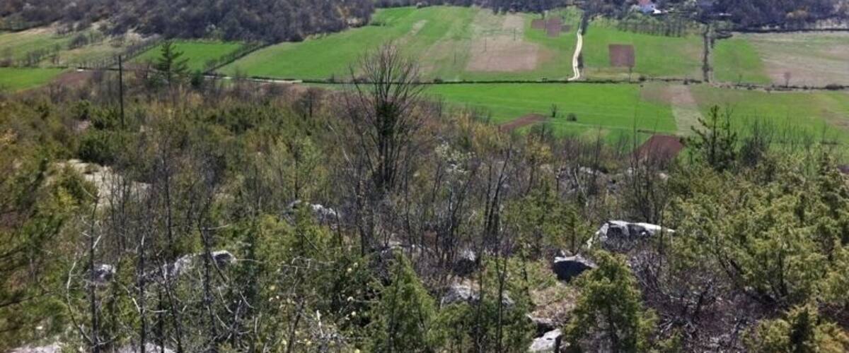 A mountainous landscape with green fields, a winding road, and a small settlement in the valley.