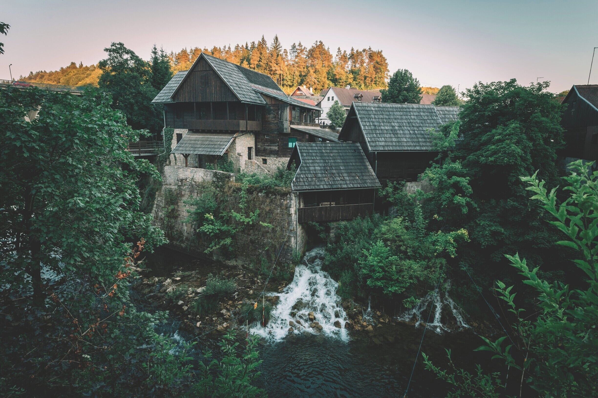 A wooden house with a stone foundation and a wooden bridge over a waterfall.