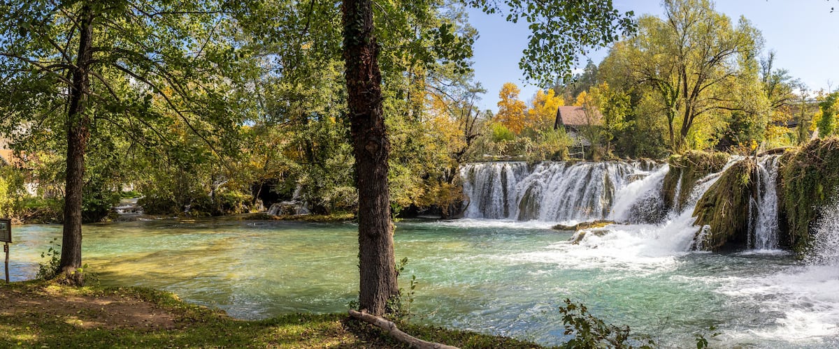 A river with clear water, surrounded by trees and a waterfall.