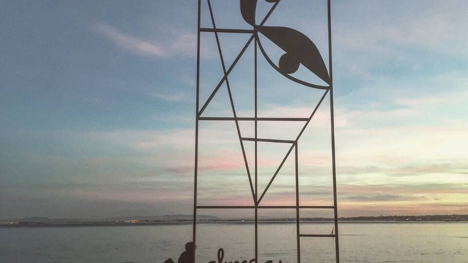 An artwork made by Almada Negreiros. In the other side of the river you can see Almada, a suburb of Lisbon with the same name as the artist