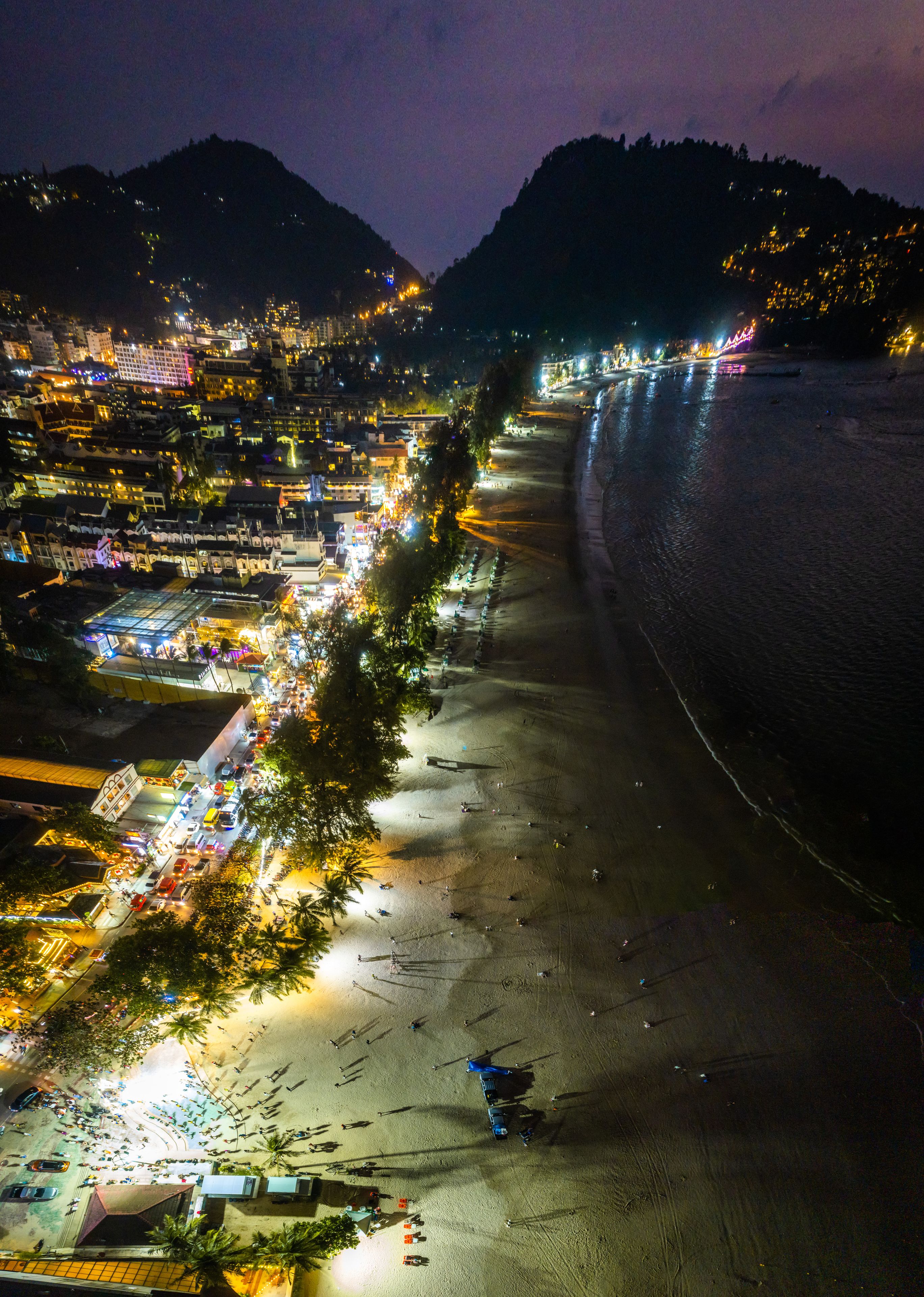 Un paisaje urbano costero nocturno con edificios iluminados y una playa.