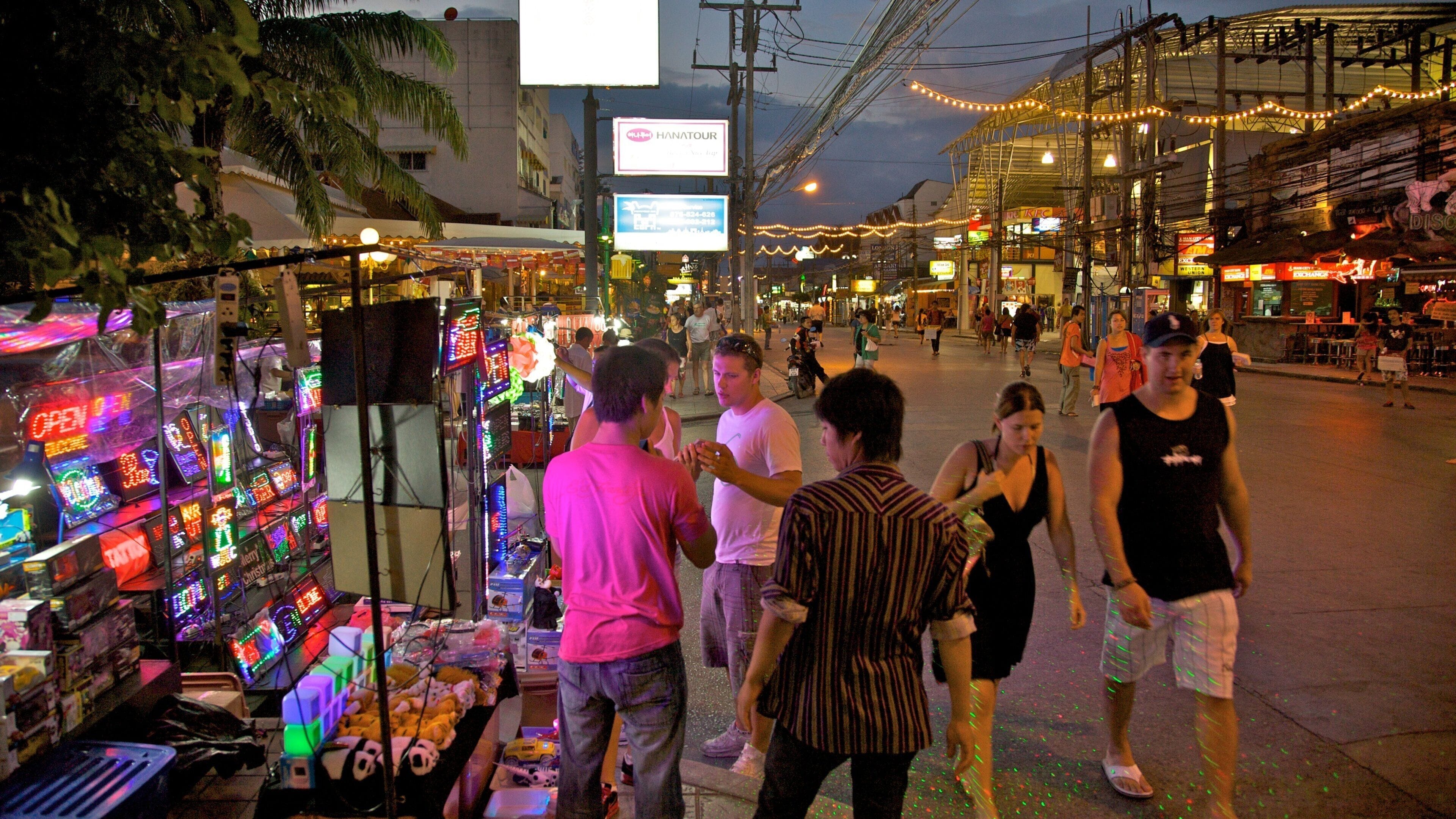 Mercado de rua movimentado à noite, com letreiros de neon e vendedores ambulantes.