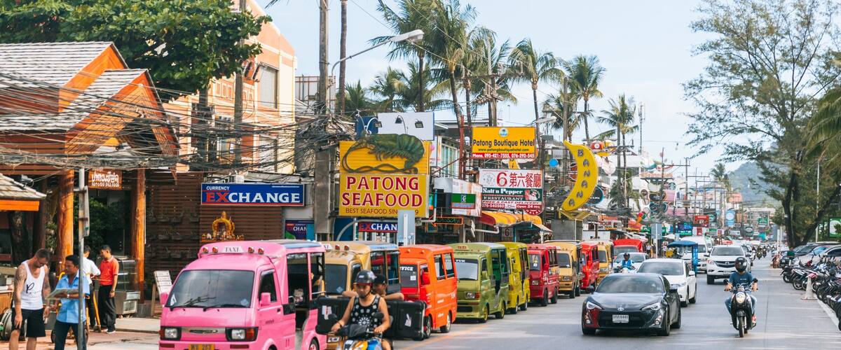 A busy street with colorful food trucks, a pink taxi, and motorcycles.