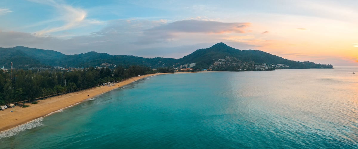A coastal landscape with a beach, a mountain, and a sunset.