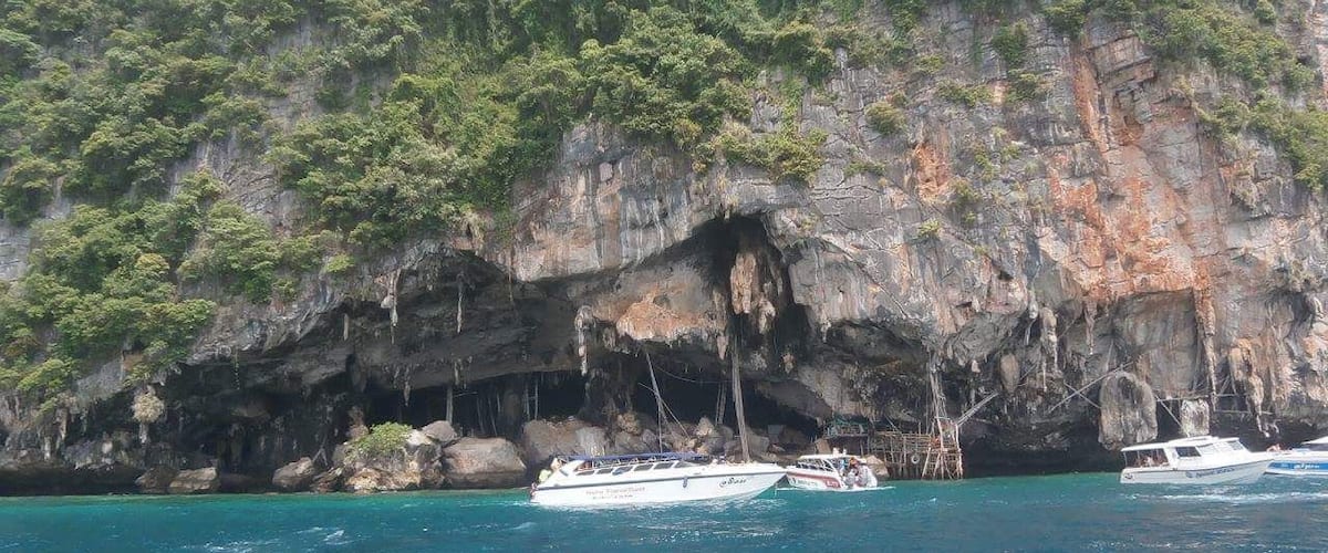 A coastal scene with a rocky cliff, clear turquoise water, and boats anchored near the shore.