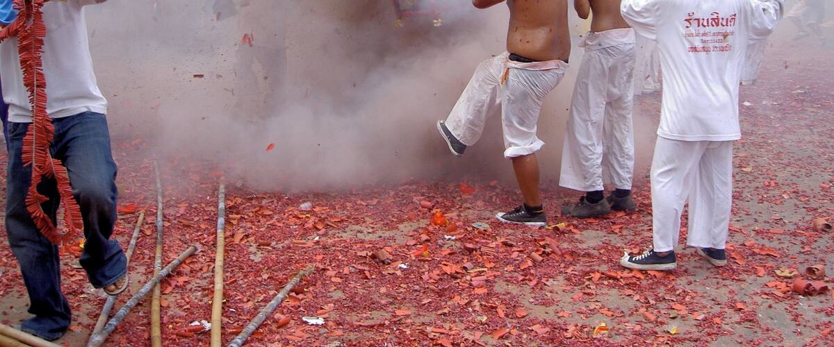 A group of people in white attire, some holding sticks, in a dusty environment with scattered leaves.