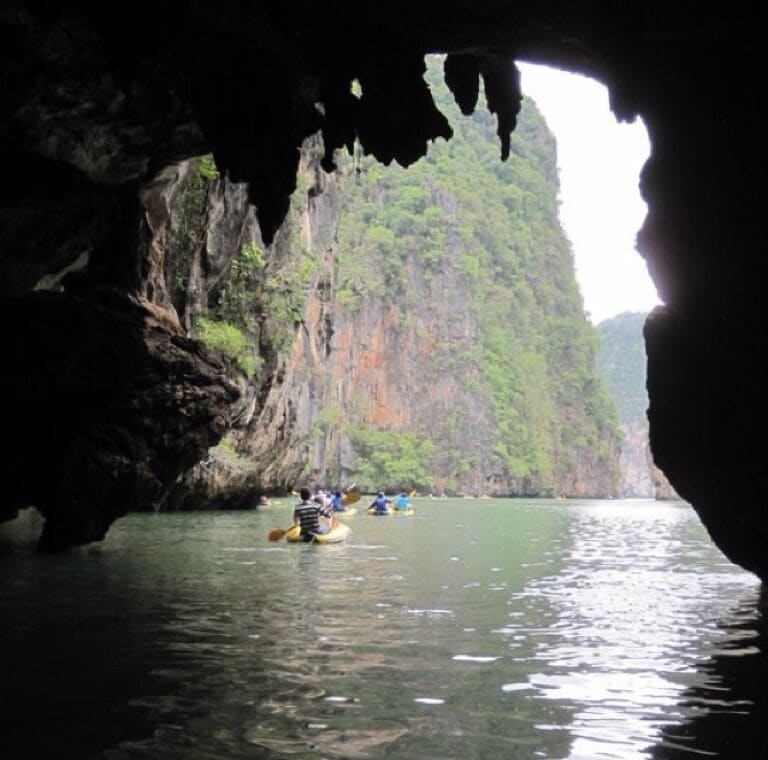 A cave opening with a river and a group of people kayaking.