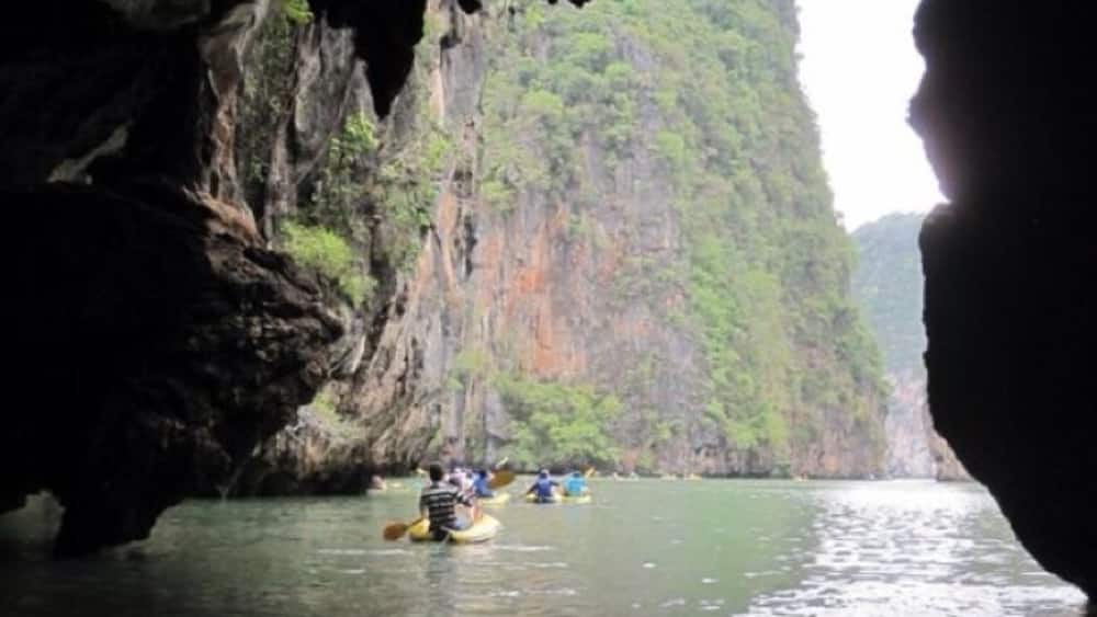 L’entrée d’une grotte, avec une rivière et un groupe de personnes pratiquant le kayak.