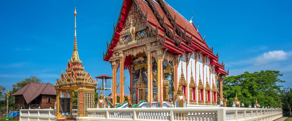 A traditional Thai temple with ornate architecture and a smaller shrine.