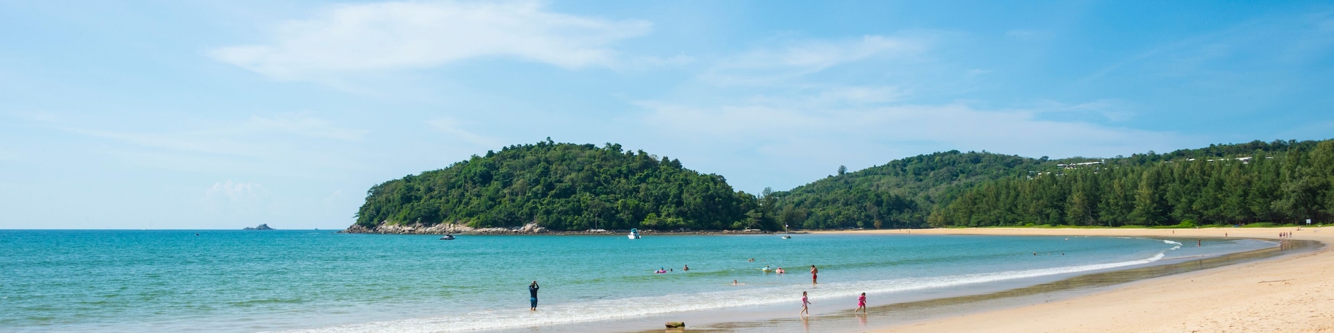 A sandy beach with clear blue water, a small island in the distance, and a few people enjoying the shore.