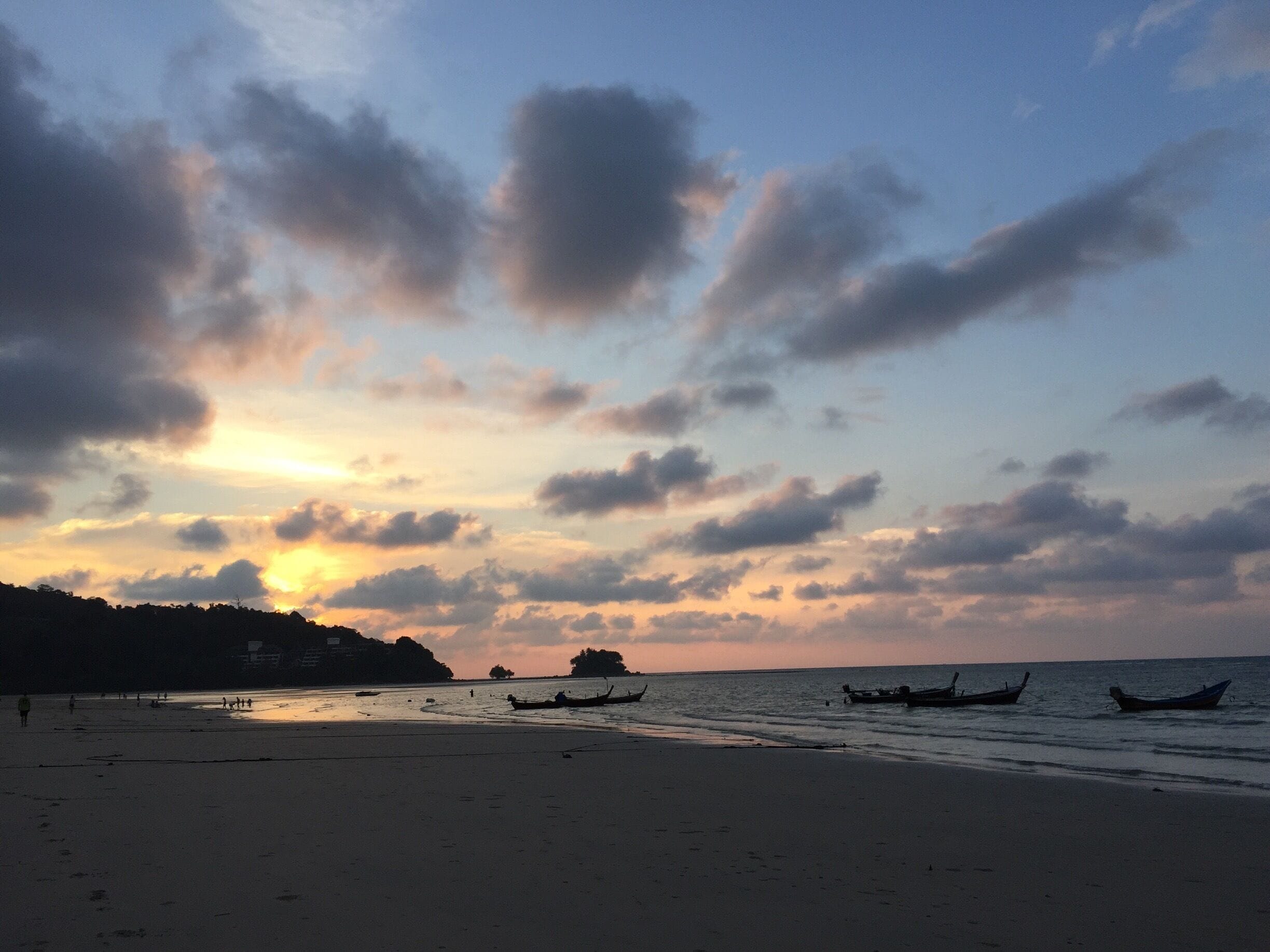 Ein Strand mit Booten und einem Sonnenuntergang.