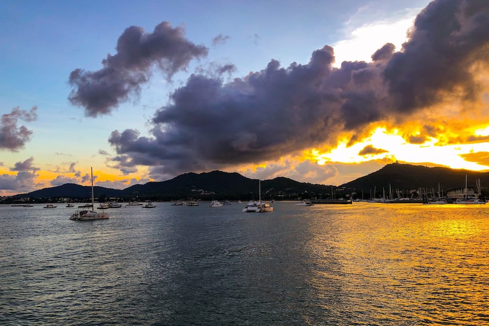 A sunset over a harbor with boats and a mountain in the background.