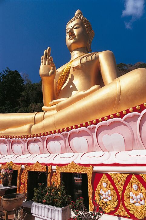 A large golden reclining Buddha statue with a white and red temple structure in the background.