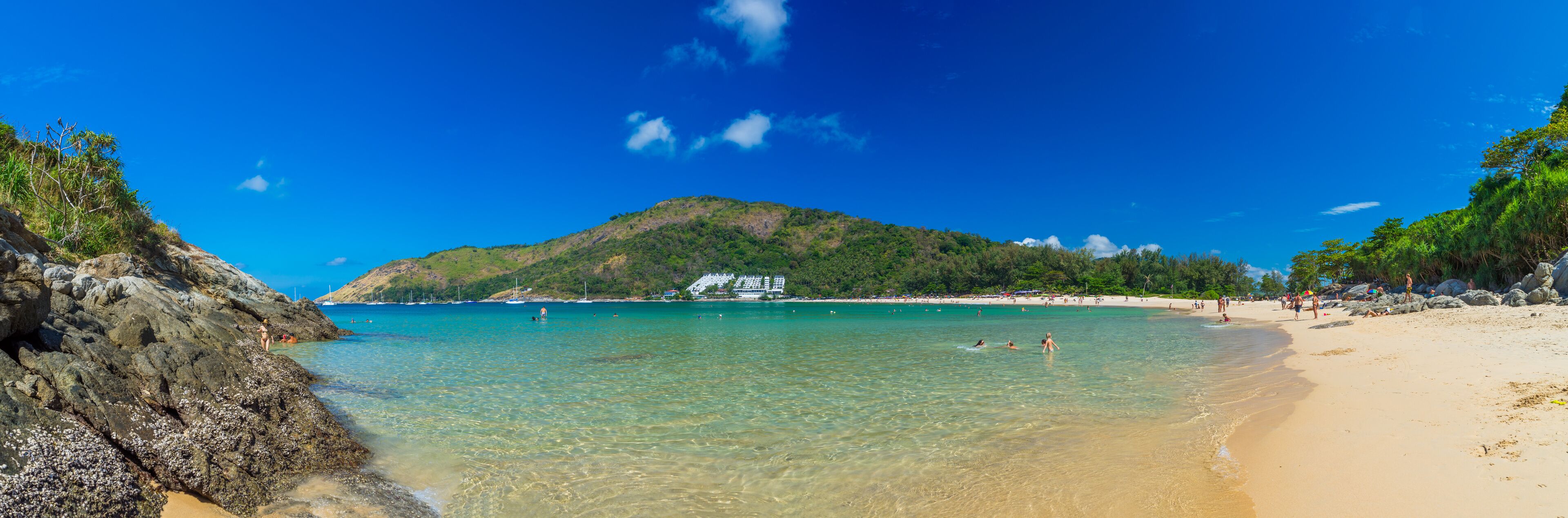 A beach with clear turquoise water, sandy shore, and a mountain in the background.