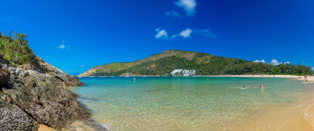 A beach with clear turquoise water, sandy shore, and a mountain in the background.