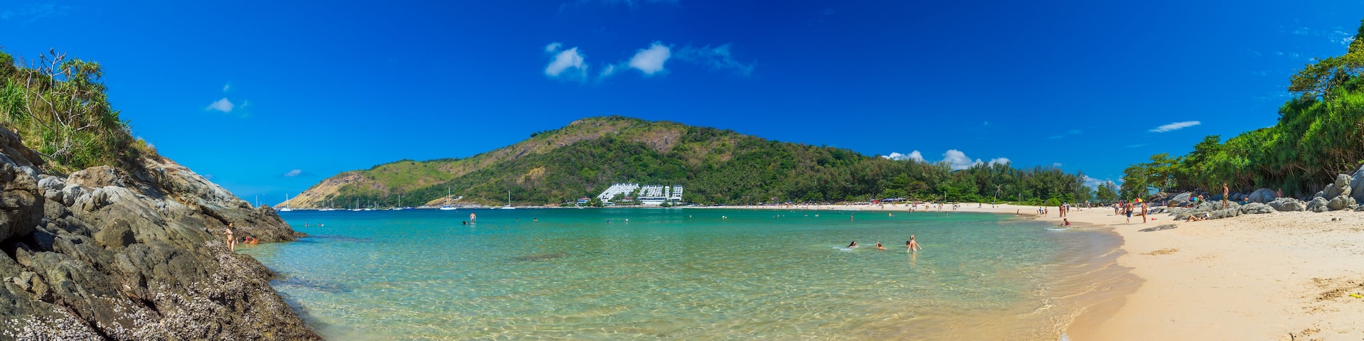 A beach with clear turquoise water, sandy shore, and a mountain in the background.