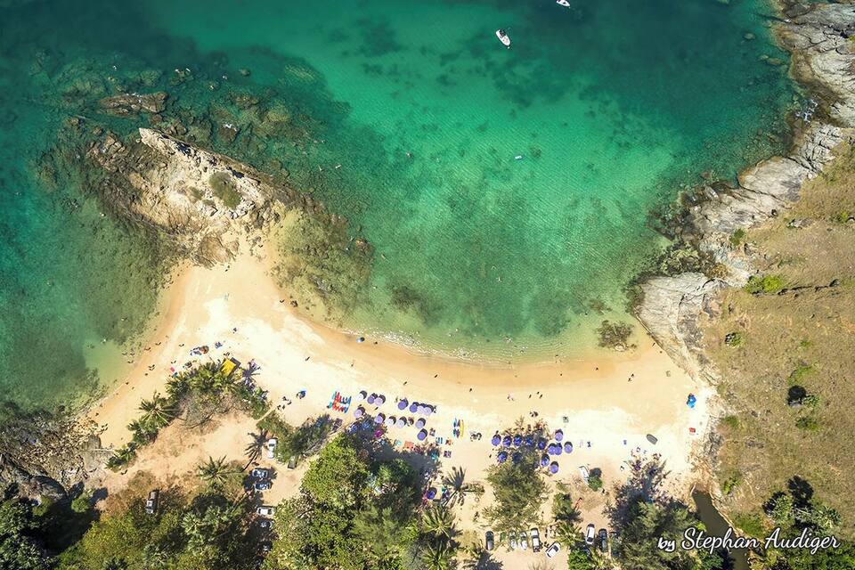 Vista aèria d'una platja amb aigües turqueses cristal·lines, sorra daurada i palmeres.