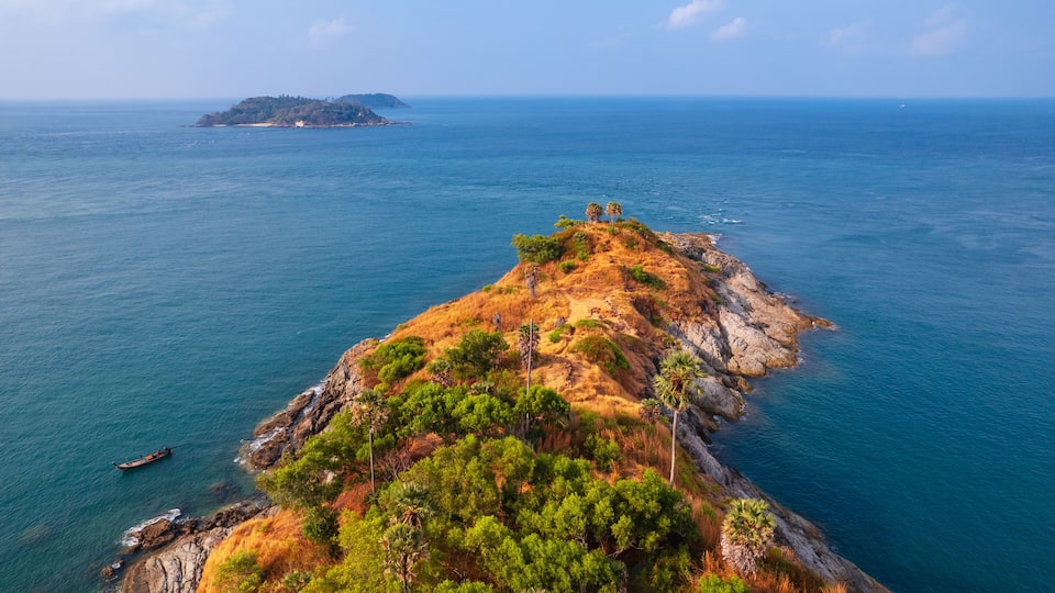 A coastal landscape with a rocky outcrop, dense greenery, and a distant island.
