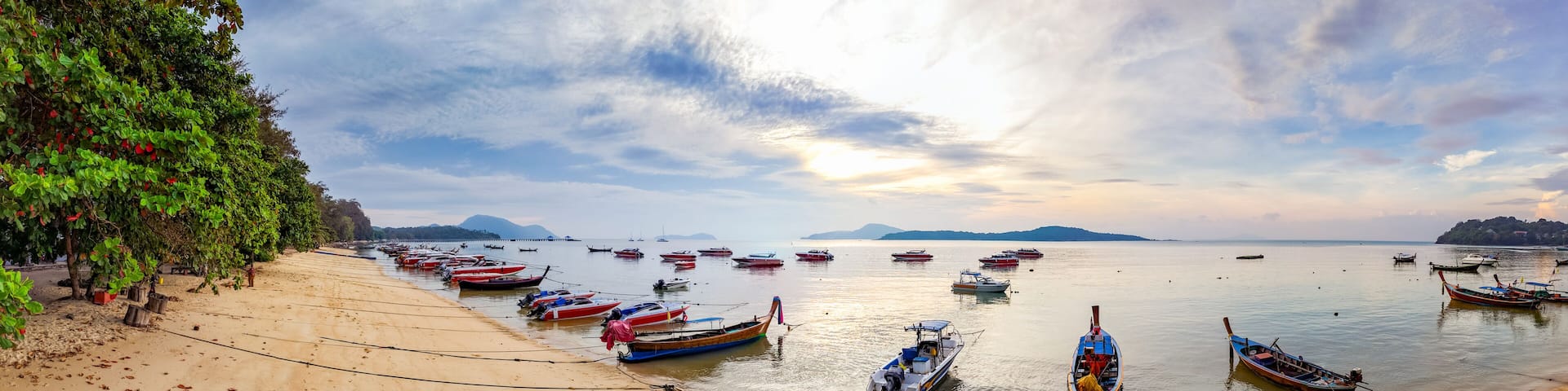 Colorful fishing boats anchored at Rawai Beach, Phuket, reflected in the calm water at dawn. Travel and tourism imagery.