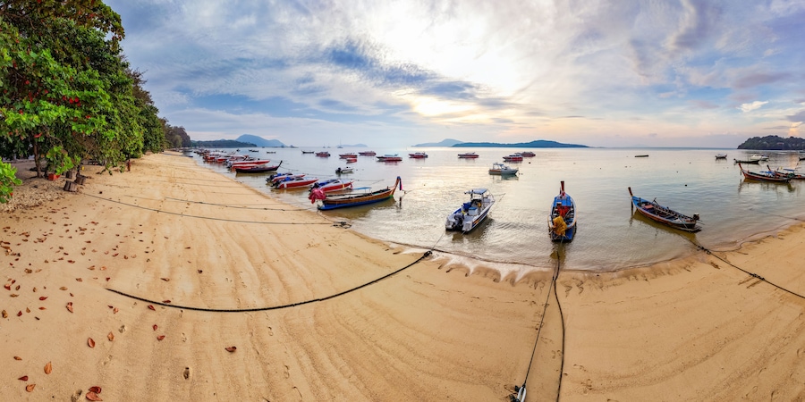 Colorful fishing boats anchored at Rawai Beach, Phuket, reflected in the calm water at dawn. Travel and tourism imagery.