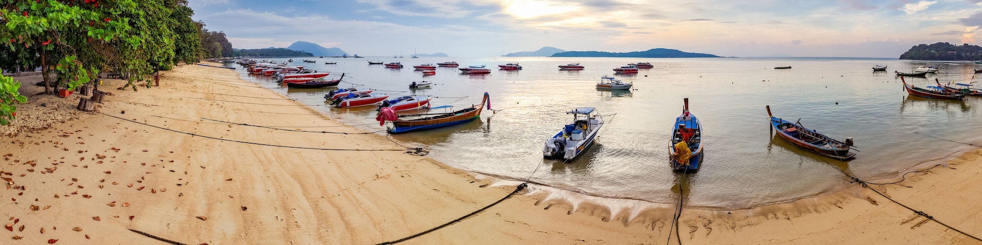 Colorful fishing boats anchored at Rawai Beach, Phuket, reflected in the calm water at dawn. Travel and tourism imagery.