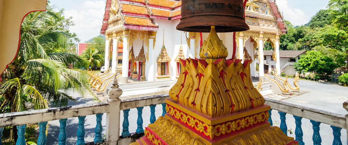A temple with a large bell, golden decorations, and a traditional Thai roof.