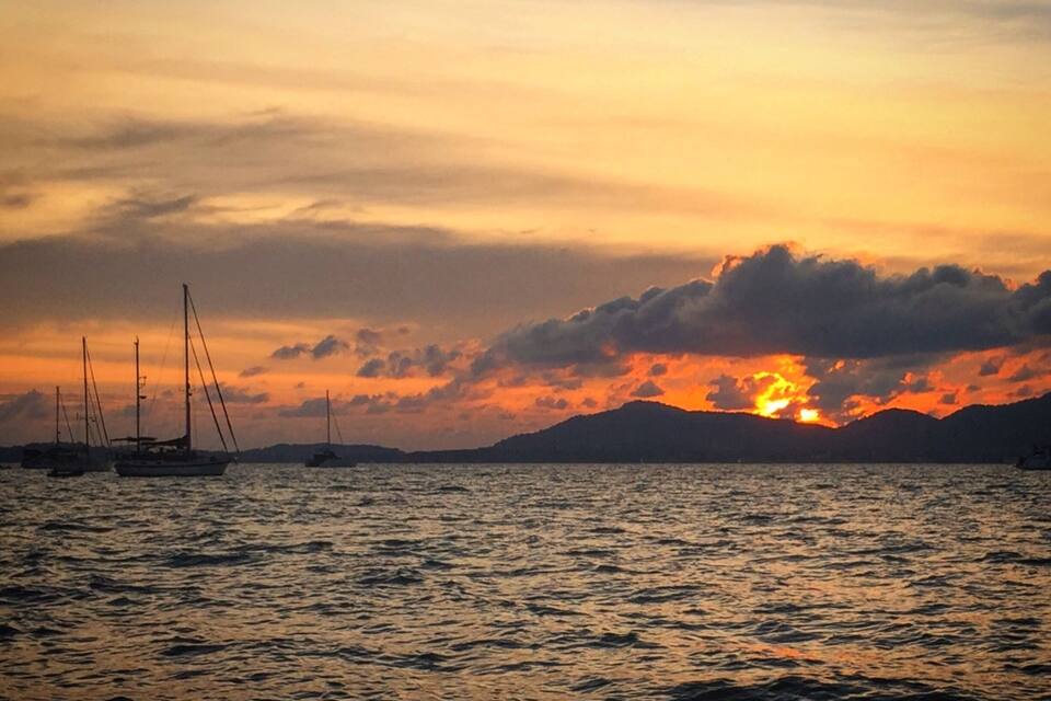 Un atardecer sobre un cuerpo de agua con veleros y montañas distantes.