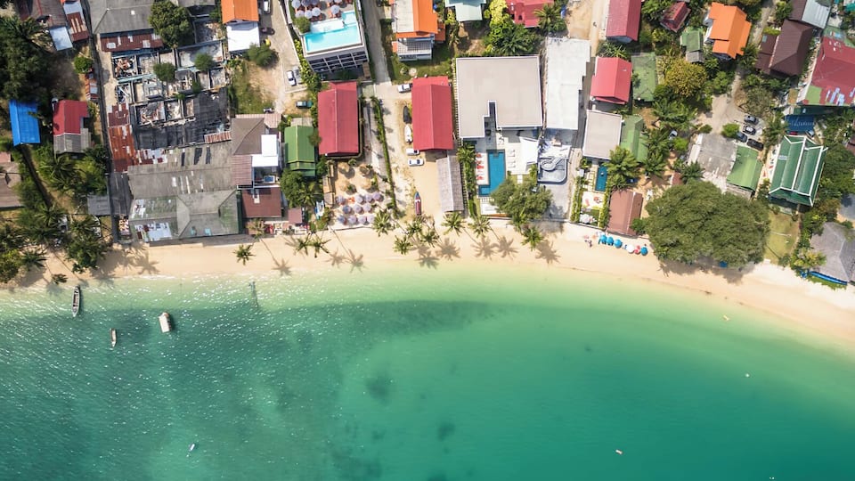 An aerial view of a coastal town with a sandy beach, colorful houses, and a clear turquoise sea.