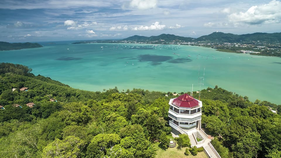A coastal landscape with a tower, lush greenery, and clear turquoise waters.
