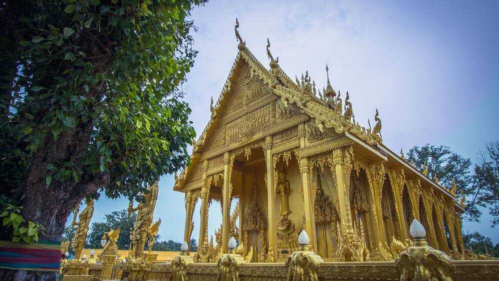 A golden temple with intricate carvings and statues, surrounded by lush greenery.