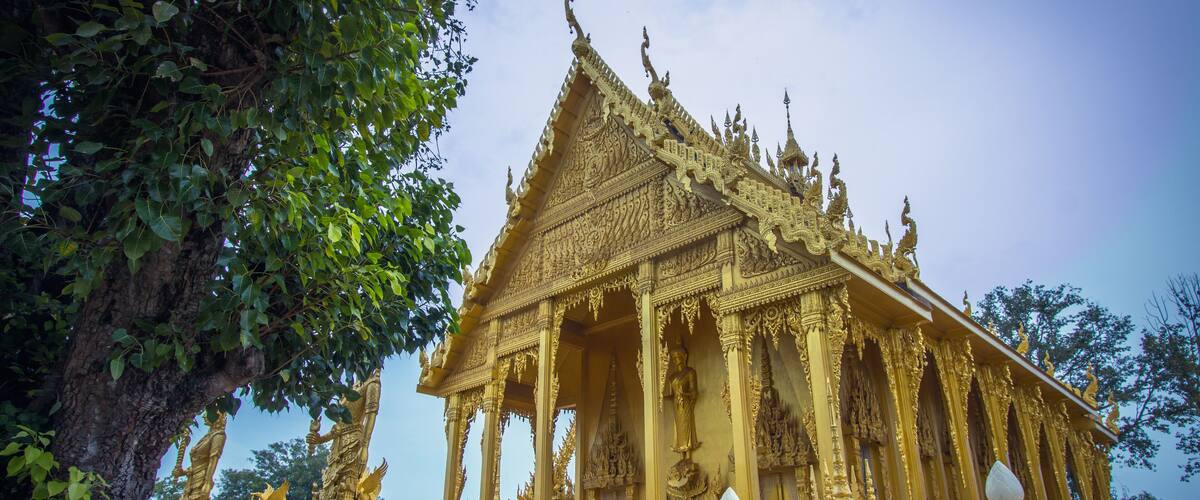 A golden temple with intricate carvings and statues, surrounded by lush greenery.