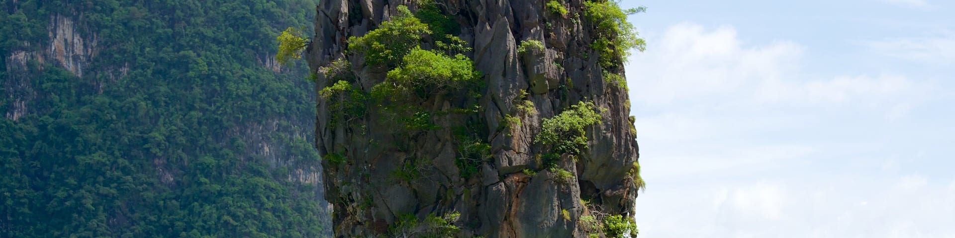 A large limestone pillar surrounded by water and lush green mountains.