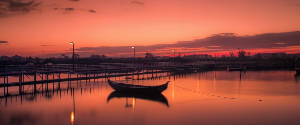 A sunset over a calm lake with a dock and a boat.