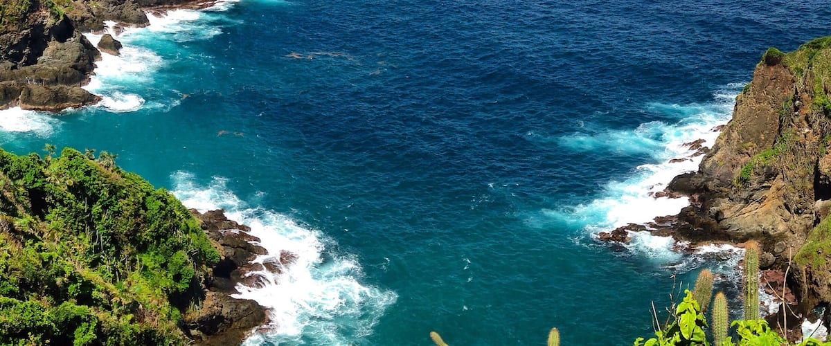 A coastal landscape with rocky cliffs, a clear blue sea, and distant islands.