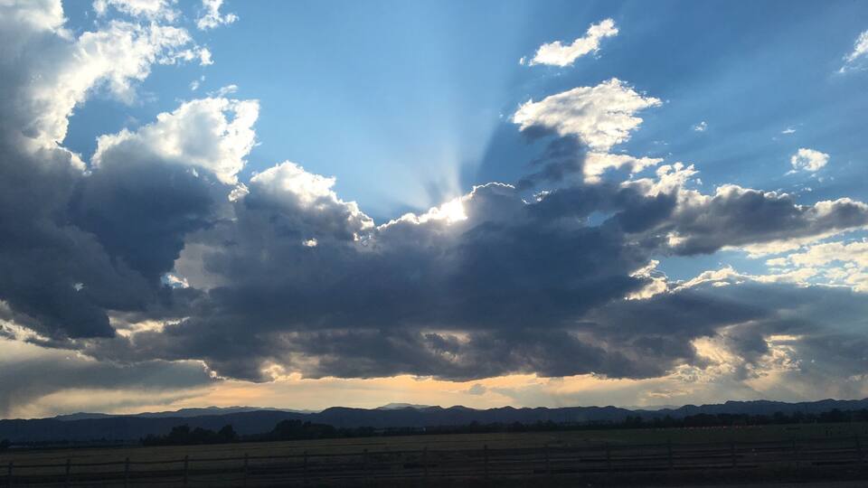 A cloudy sky with rays of sunlight breaking through, a road, and distant mountains.
