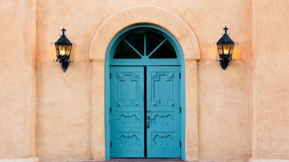 A turquoise double door with decorative patterns, flanked by two black wall-mounted lanterns.